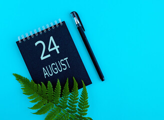 August 24th. Day 24 of month, Calendar date. Black notepad sheet, pen, fern twig, on a blue background. Summer month, day of the year concept