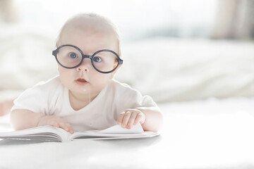 A newborn baby is lying on a soft bed in glasses.