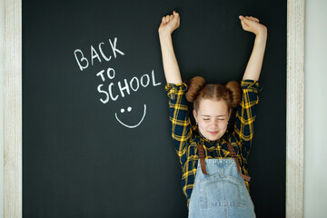Happy smiling girl. Child at the blackboard. Girl indoor classroom with chalkboard on background. We return to school. High quality photo
