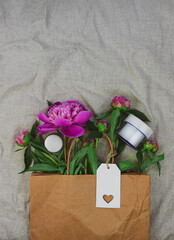Cream jar mockup pink peony flowers in kraft paper bag on lilnen fabric background.Natural skincare moisturizer cosmetic, healthy skin SPA wellness facial body hydration Female treatment shopping sale