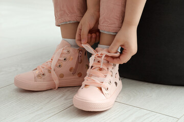 Little girl tying shoe laces at home, closeup - Powered by Adobe