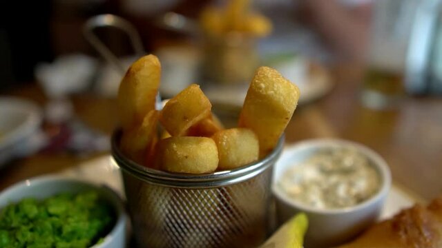 Gastro pub meal of fish and chips. Slow motion footage of close up of chunky English traditional battered fish, mushy peas and chips with tartare sauce and lemon wedge. Restaurant setting