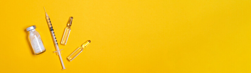 Syringe and vaccine or medicine vial on a yellow background with copy space for immunization...