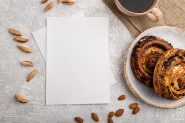 White paper invitation card, mockup with almonds, bun, cup of coffee, linen textile on gray concrete background. flat lay, copy space.