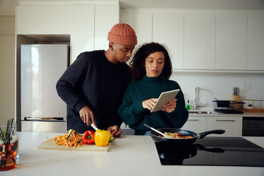Young mixed race couple cooking food in the kitchen and using a tablet. Couple looking at tablet for food recipe. High quality photo