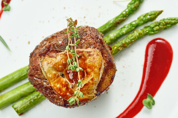 Portion of grilled mignon steak with foie gras and asparagus, berry sauce in a white plate....