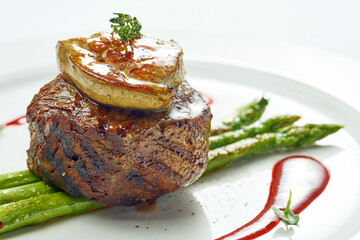 Portion of grilled mignon steak with foie gras and asparagus, berry sauce in a white plate....
