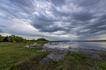 Obraz premium Evening landscape, The dramatic sky is reflected in the water. Green spring grass in the foreground.