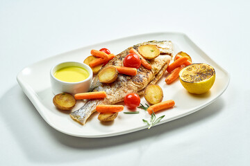 Grilled dorado with potatoes, carrots, and cherry tomatoes in a white plate. Isolated on white background. View from above