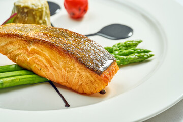 Grilled salmon steak with asparagus and balsamic sauce in a white plate. Isolated on white background. View from above