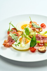 Delicious breakfast - fried egg with bacon, mix salad, asparagus and cherry tomatoes in a white plate. Isolated on white background.