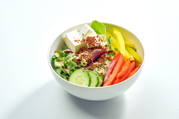 Delicious veggie bowl with cucumber, bell pepper, salad mix, quinoa and tofu in a white plate. Isolated on grey background.