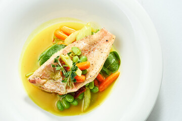 Fried Sea bass fillet with stewed vegetables and orange sauce in a white plate. Isolated on grey background.