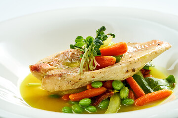 Fried Sea bass fillet with stewed vegetables and orange sauce in a white plate. Isolated on grey background.