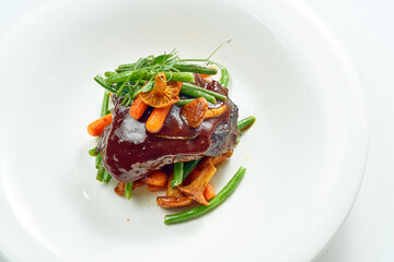 Beef cheek steak, caramelized in wine sauce with chanterelles and asparagus in a white plate. Isolated on grey background.