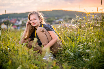Obraz na płótnie Canvas Portrait of a teenage girl with backpack traveling on summer evening against the backdrop of landscape and sunset.