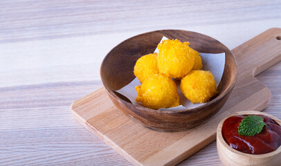 Cheese ball and ketchup tomato sauce in wooden bowl on cutting board, on wooden table background. Unhealthy junk food, High fat and calories.
