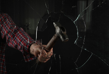 Man breaking window with hammer on black background, closeup