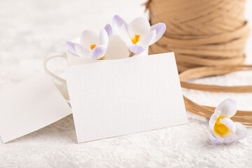 White paper invitation card, mockup with purple crocus snowdrop flowers on gray concrete background. side view, copy space.