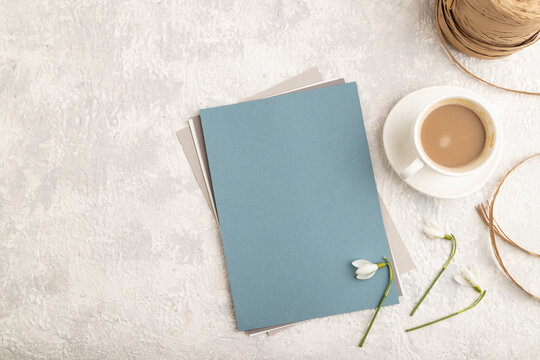 Blue paper sheet mockup with spring snowdrop galanthus flowers and cup of coffee on gray concrete background. top view, copy space.