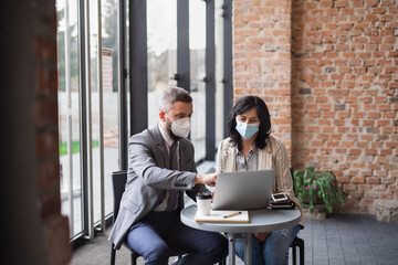 Portrait of businesspeople sitting at the table and working indoors, coronavirus concept.