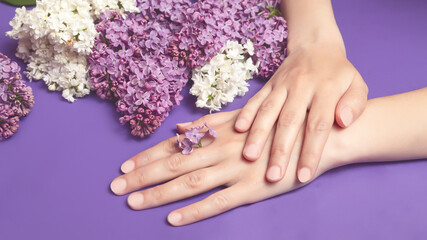 Fototapeta premium Close-up of beautiful sophisticated female hands with pink lilac flowers on a white background. Hand care concept, anti-wrinkle, anti-aging cream, spa