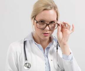 Portrait of a female family doctor wearing glasses in doctor's overall with stethoscope looking seriously