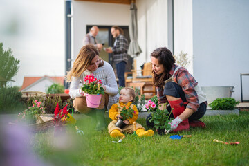Happy multigeneration family outdoors planting flowers in garden at home, gardening concept.