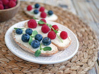 Sweet bruschetta with cream cheese and fresh berries. Homemade healthy breakfast with bread, cheese, blueberries and raspberries. Three delicious sandwiches on a plate