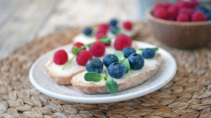 Sweet bruschetta with cream cheese and fresh berries. Homemade healthy breakfast with bread, cheese, blueberries and raspberries. Three delicious sandwiches on a plate