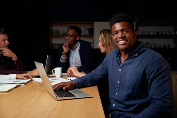 Portrait of smiling young african male team leader with laptop looking at camera while his...