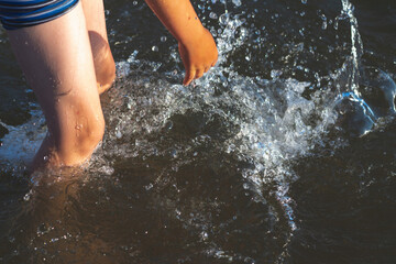Young kid play in water and making splash boy to prepare in lake or river and have fun with drops.Closeup.