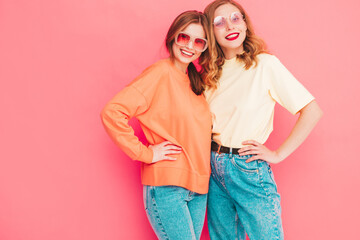 Two young beautiful smiling hipster female in trendy summer hipster  clothes. Sexy carefree women posing near pink wall in studio. Trendy and positive models having fun. Cheerful and happy