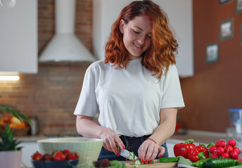 Beautiful redhair young woman is preparing vegetable salad in the kitchen.