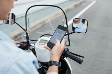 Over shoulder view of man in wristwatch driving moped and using smartphone while navigating with online app