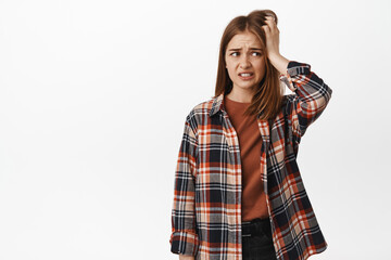 Worried and anxious blond girl scratch head, looking aside and panicking, feel nervous or...