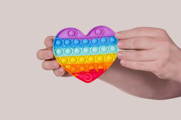 A young guy holds a rainbow heart in his hands. New fashion colorful silicone antistress Pop It toy