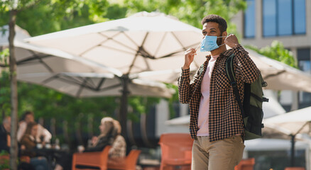 Portrait of happy young man taking off face mask outdoors in city, covid-19 concept.