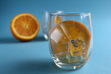 cooking lemonade with orange. step-by-step instructions. Step 1 pour into a glass of ice and put a piece of orange. Glass of ice and fruit orange on a blue background with a place for text