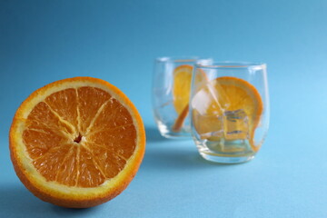 cooking lemonade with orange. step-by-step instructions. Step 1 pour into a glass of ice and put a piece of orange. Glass of ice and fruit orange on a blue background with a place for text