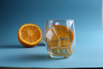 cooking lemonade with orange. step-by-step instructions. Step 1 pour into a glass of ice and put a piece of orange. Glass of ice and fruit orange on a blue background with a place for text