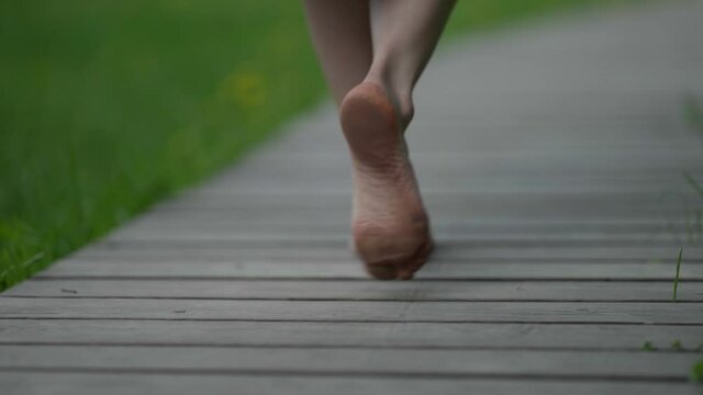 barefooted woman is walking on wood path in park at summer day, closeup of feet
