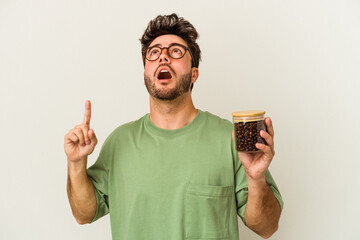 Young caucasian man holding a coffee jar isolated on white background pointing upside with opened mouth.