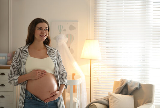 Happy pregnant woman touching her belly indoors