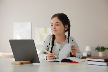Little girl doing homework with modern tablet at home