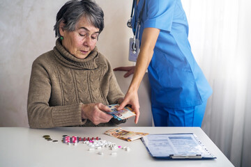 An elderly woman, a retired woman, is counting money, her savings and putting aside some of it for medicine and treatment. A young doctor collects money for her services.