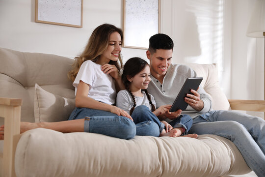 Happy family with little daughter using tablet on sofa in living room