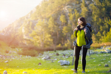 A young girl with a backpack and travel equipment looks at the amazing sunset in the mountains while she hikes along the trail. A traveler walks through the national park.