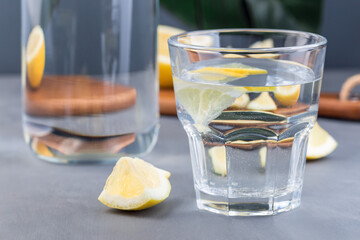 Optical illusion lemon distorted through the glass of water, lemon water or lemonade, monstera leaf on gray background, horizontal