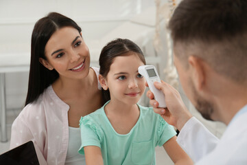 Mother with daughter visiting pediatrician in hospital. Doctor measuring little girl's temperature